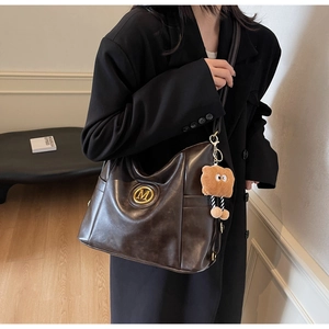 Detail of dark brown leather tote bag with gold M logo and teddy bear charm
