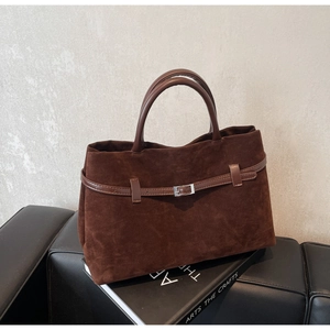 Close-up of matte brown suede tote bag with decorative silver buckle and leather straps