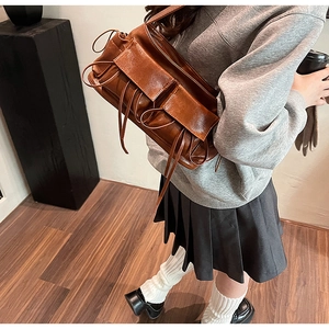 Detailed view of brown bow-pleated shoulder bag with glossy synthetic leather texture