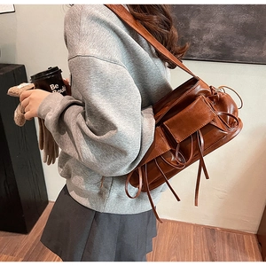 Brown pleated shoulder bag with decorative ties shown on a model in a minimal setting