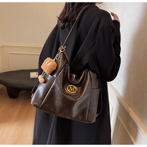 Detail of dark brown tote bag showing gold M logo and cute plush bear charm on the strap
