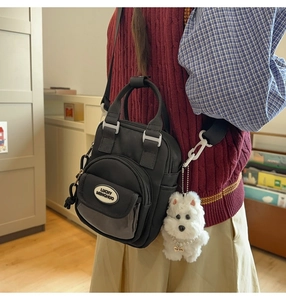 Detail of black nylon mini crossbody bag with a white dog plush charm and adjustable strap