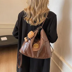 Retro brown leather hobo bag with gold M logo and teddy bear charm on model back