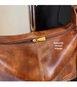 Détail de la fermeture éclair en métal doré et du cuir huilé marron du sac à bandoulière