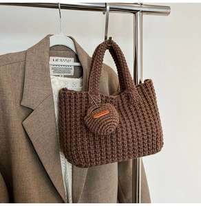 Detail of a brown knit bucket bag showing vertical textures and a Hand Made charm