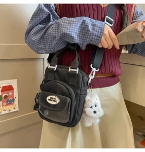 Detail of black nylon crossbody bag with Lucky Menghuo logo and plush puppy charm