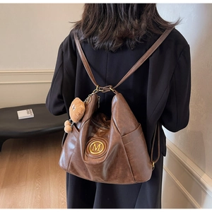 Brown vintage leather backpack with golden M logo and plush bear charm shown on model
