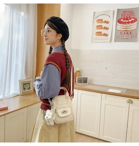 Detail of white mini crossbody bag featuring front pocket and cute plush puppy charm