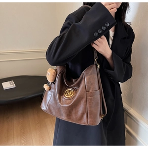 Detail view of large brown vintage tote bag with gold M logo and teddy bear charm