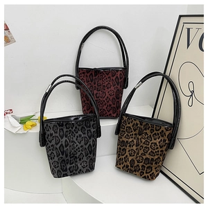 Three leopard print bucket bags in burgundy, gray, and brown on a minimalist display