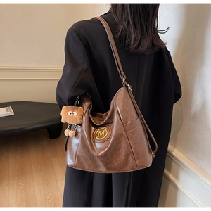 Close-up of brown vintage hobo bag with gold M logo and cute plush monster charm