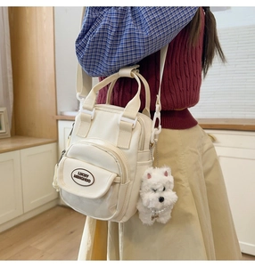 Detail of white canvas crossbody bag featuring front pocket and plush dog charm