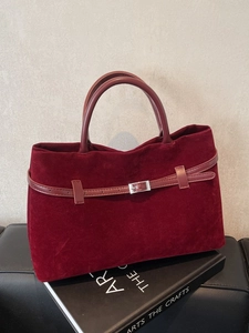 Retro burgundy velvet tote bag with leather strap detail on a stylish art book backdrop