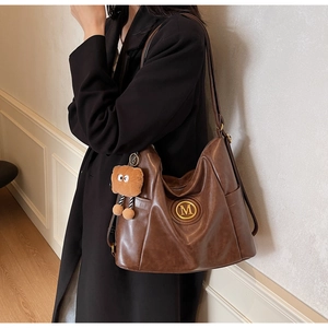 Detail of vintage brown leather tote bag with gold M logo and cute bear charm pendant