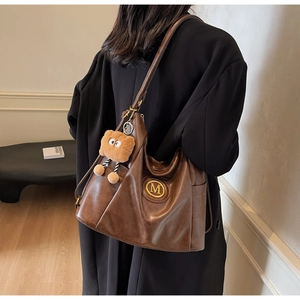 Side view of a vintage large capacity brown tote bag with a golden M logo and plush charm