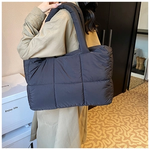 Detail of dark grey quilted puffer tote bag with thick padded handles on shoulder