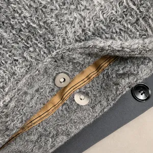 Detail van de zilveren magnetische sluiting en zwarte knoop op de grijze imitatiebont tas