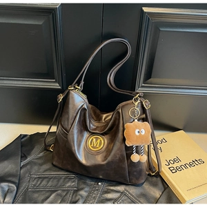 Close-up of retro dark brown leather tote bag with gold M logo and plush pendant accessory