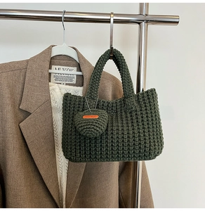 Detail of dark green knit tote bag with heart-shaped handmade charm on a clothes hanger