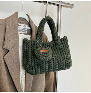 Detail of dark green hand-knitted tote bag with crochet heart charm and leather tag