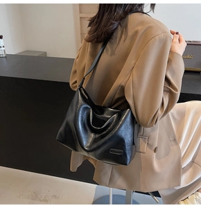 Détail d'un sac cabas noir brillant avec plaque logo métallique et texture cuir lisse