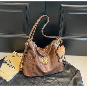 Detail of vintage brown leather shoulder bag with a metal M logo and plush bear charm