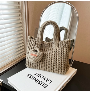 Close-up of beige knit tote bag with vertical texture and Hand Made leather tag charm