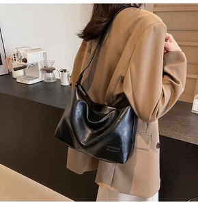 Détail du sac bandoulière noir brillant avec plaque logo en métal sur similicuir texturé