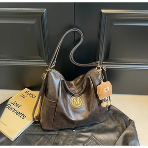 Detail of vintage dark brown tote bag with M logo and cute plush charm on wood background