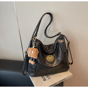 Detail of black leather tote bag with gold M-logo and brown plush cartoon charm