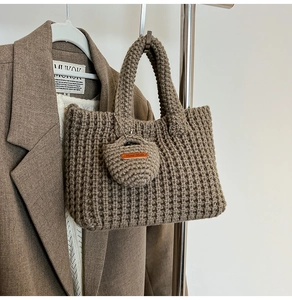 Detail of brown knit bucket bag with Hand Made charm against a stylish blazer
