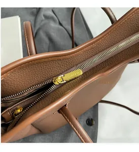 Close-up of golden metal zipper with SOUKU logo on brown lychee grain leather bag
