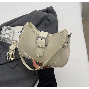 Detail view of beige underarm saddle bag with silver buckle on grey blazer backdrop