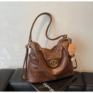 Detail of vintage brown leather tote bag with gold M logo and cute bear charm