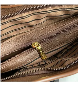 Close-up of brown pebbled leather bag interior with striped lining and gold logo zipper