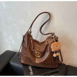 Close-up of vintage brown leather tote bag featuring gold M logo and plush monster charm