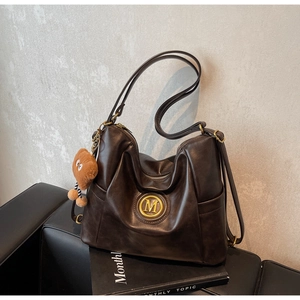 Detail view of a vintage dark brown leather tote with M-logo and plush charm on a sofa