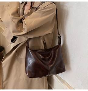 Vue détaillée du sac bandoulière marron foncé brillant sur un mannequin en trench beige