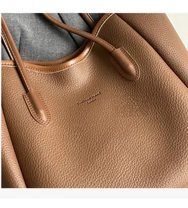 Detailed close-up of brown litchi grain leather texture and handle stitching on tote bag