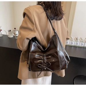 Detail of dark brown glossy bag featuring bow design and contrast white stitching