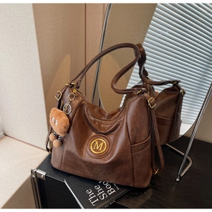 Detailed shot of brown vintage PU leather tote featuring a gold M logo and bear charm