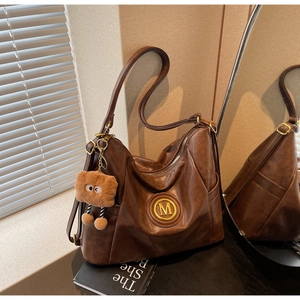 Detail of dark brown leather hobo bag with gold metal logo and plush bear charm