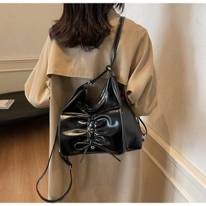 Detail of black patent leather shoulder bag with bow element and white contrast stitching