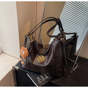 Detail of dark brown leather tote bag with gold M logo and cute bear pendant on a cabinet