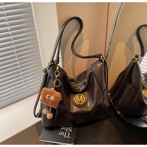Close-up of brown faux leather tote with vintage M logo and cute plush monster charm