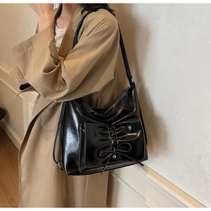 Detail of glossy black patent leather shoulder bag with pleated bow and contrast stitching