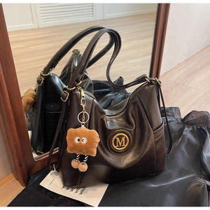 Detail view of large dark brown leather tote bag with gold M logo and plush charm