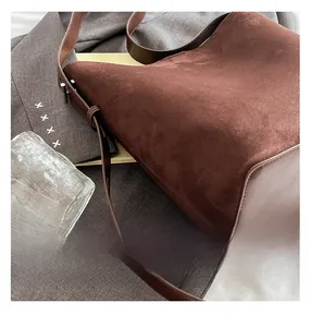 Detail of dark brown suede bucket bag with adjustable leather strap and metal buckle