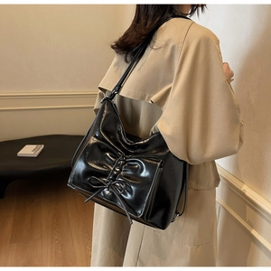Detail of black glossy leather tote bag with white stitching and decorative bow tie