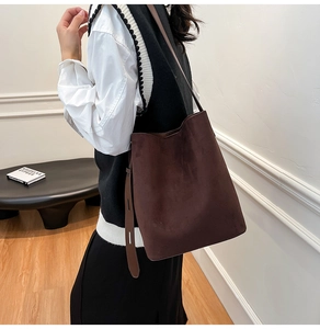 Detail view of large dark brown suede bucket bag with wide strap on shoulder
